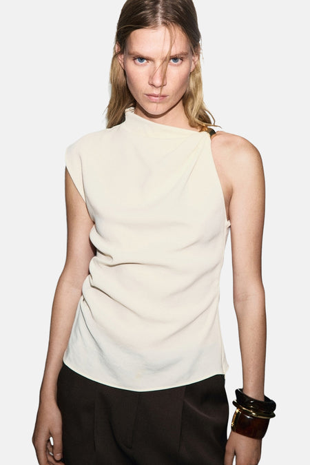 Ecru mouwloos blouse van MANGO, gedragen met een bruine wijde broek en een donkere armband.