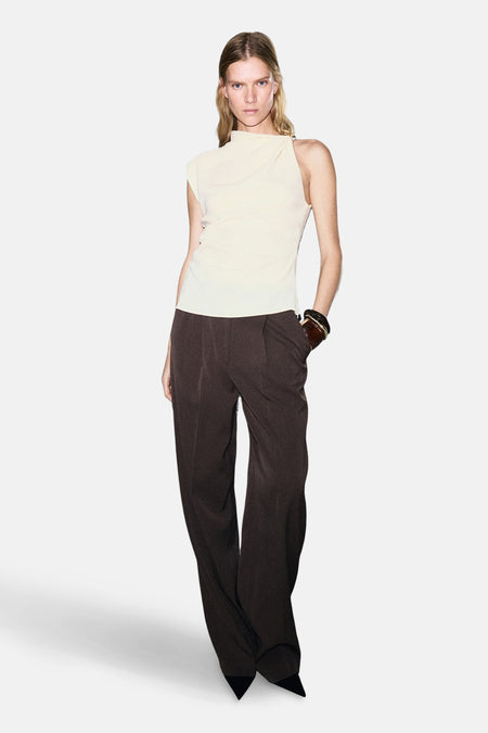 Chemisier écru sans manches de MANGO, porté avec un pantalon marron ample et un bracelet en cuir.