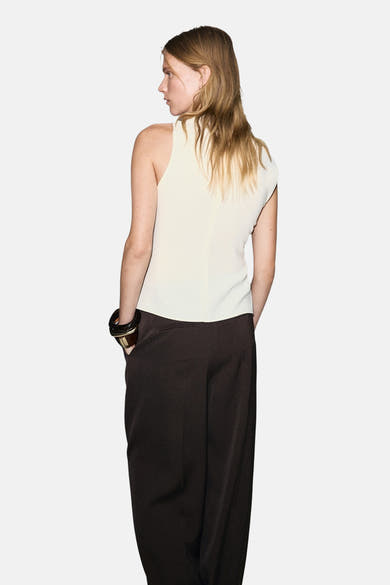 Blouse écrue sans manches de MANGO, portée avec un pantalon ample marron et un bracelet foncé.