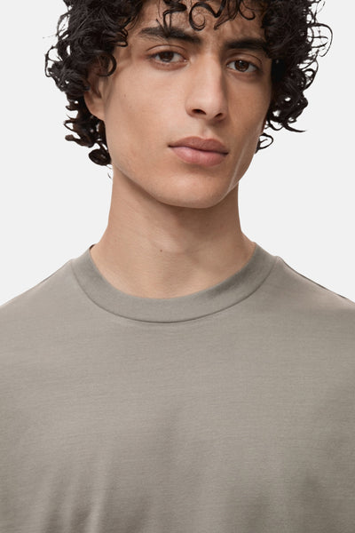 Grijze T-shirt met korte mouwen van MANGO, effen, gedragen door een man met krullend haar.
