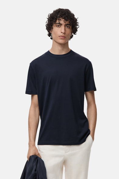 Blauw T-shirt met korte mouwen van MANGO, gedragen met een beige broek en een bijpassend jasje in de hand.