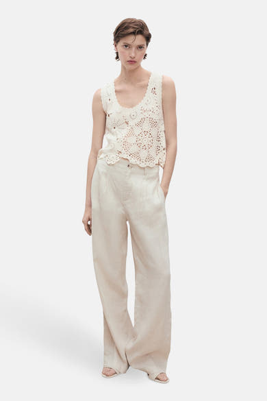 Ecru mouwloos topje van MANGO, versierd met ingewikkelde gehaakte patronen en gedragen met een beige wijde broek.
