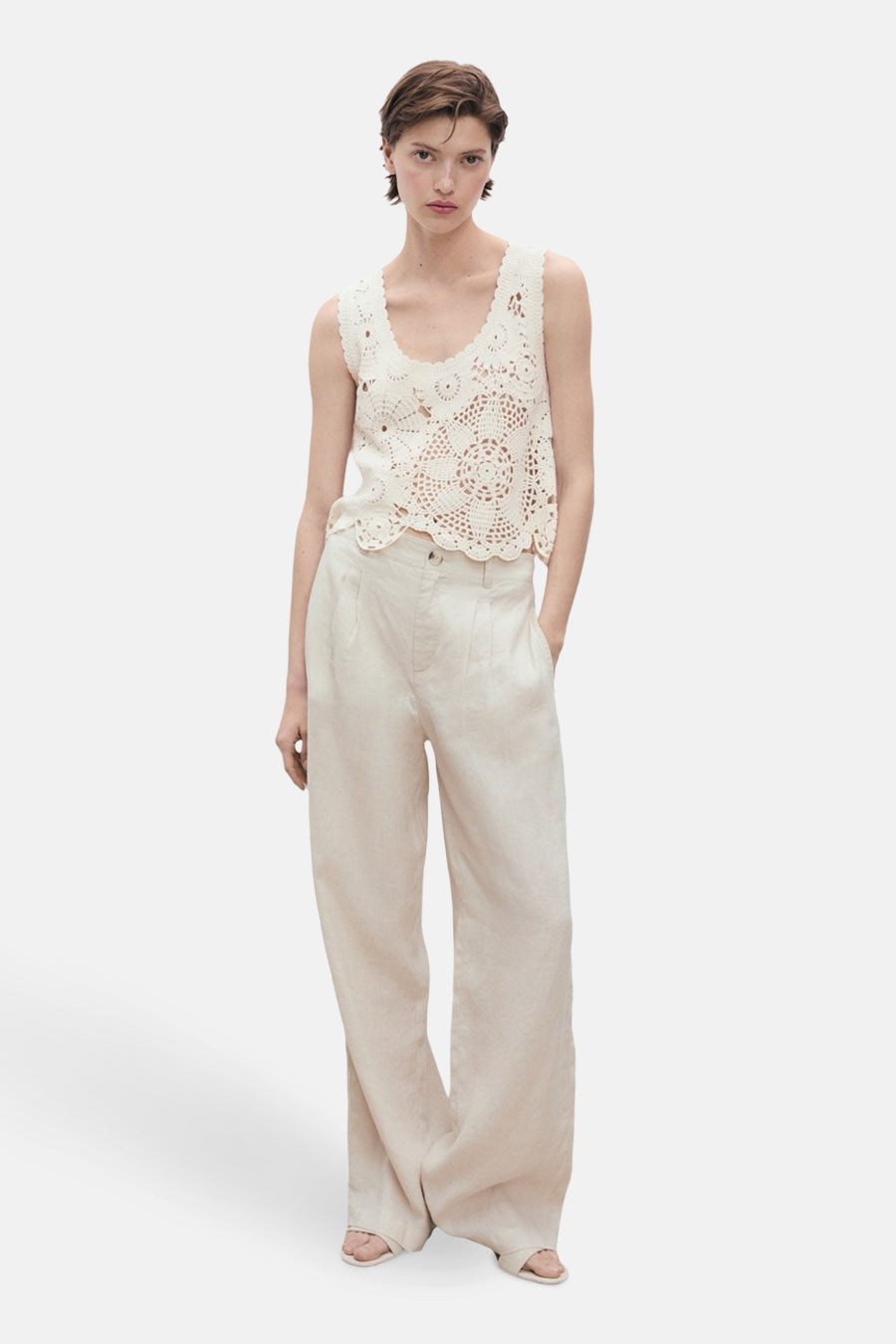 Ecru mouwloos topje van MANGO, versierd met ingewikkelde gehaakte patronen en gedragen met een beige wijde broek.