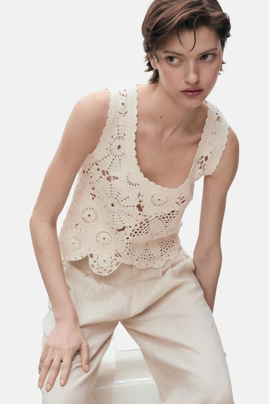 Ecru mouwloos topje van MANGO, met ajour gehaakt patroon, gedragen met een beige broek.