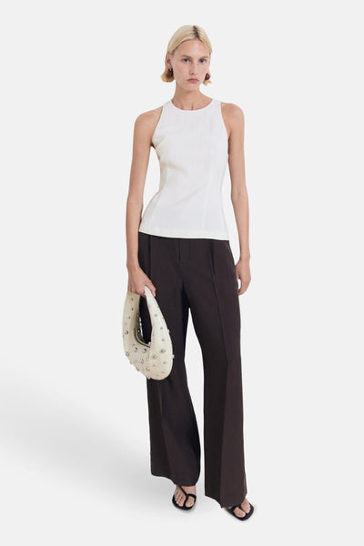 Ecru mouwloos overhemd van MANGO, met bruine broek met rechte pijpen en witte tas met zilveren studs.