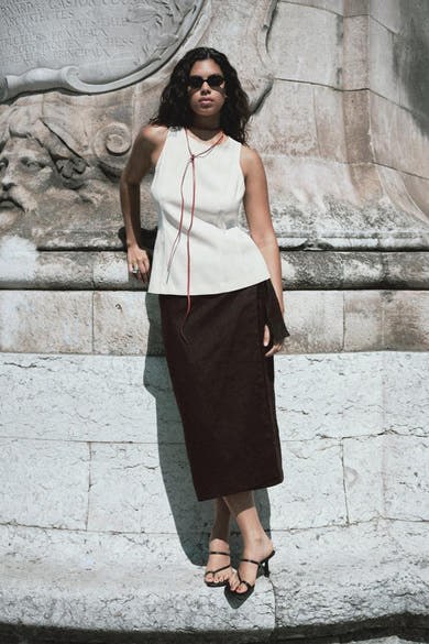 Ecru blouse van MANGO met rode strikjes, gedragen met een bruine rok en zwarte hakken.