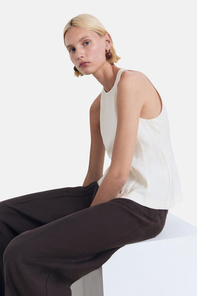 Crèmekleurige mouwloze blouse van MANGO, gedragen met een bruine broek op een witte achtergrond.