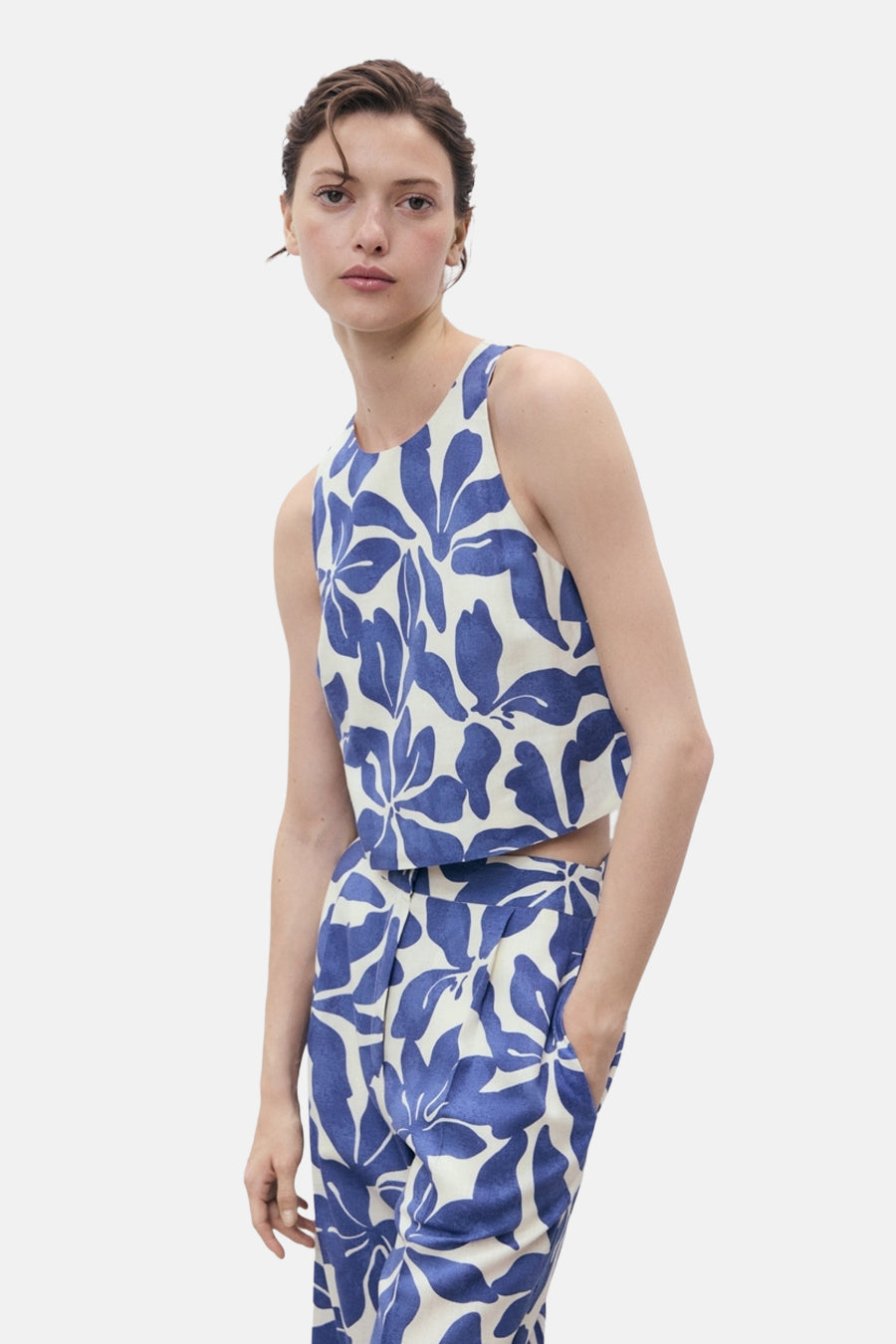 Blauwe broek met bloemenprint van MANGO, gedragen met een bijpassend topje, één hand in de zak.