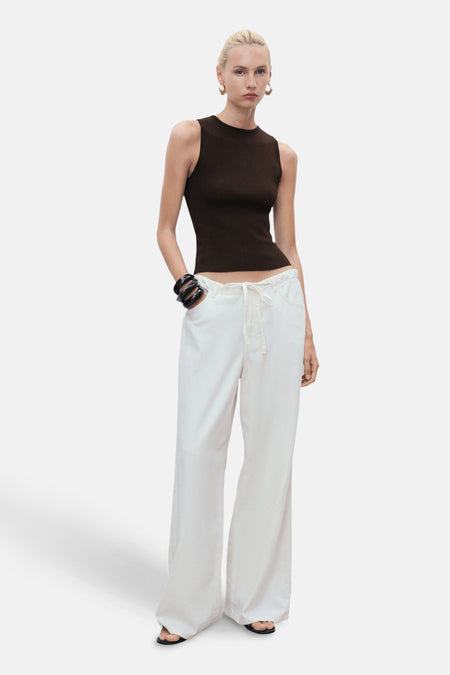 Bruin mouwloos topje van MANGO, gedragen met een witte broek met hoge taille en sandalen.