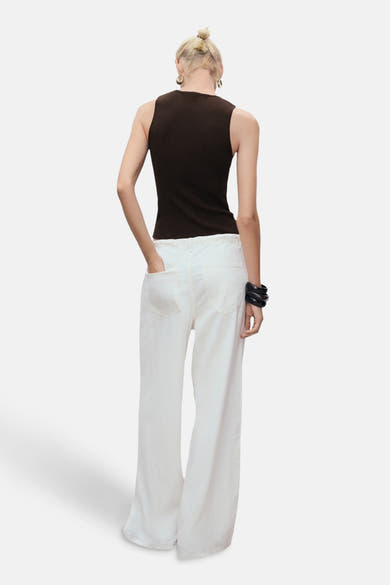 Top sans manches brun de MANGO, porté avec un pantalon blanc large et un bracelet noir.
