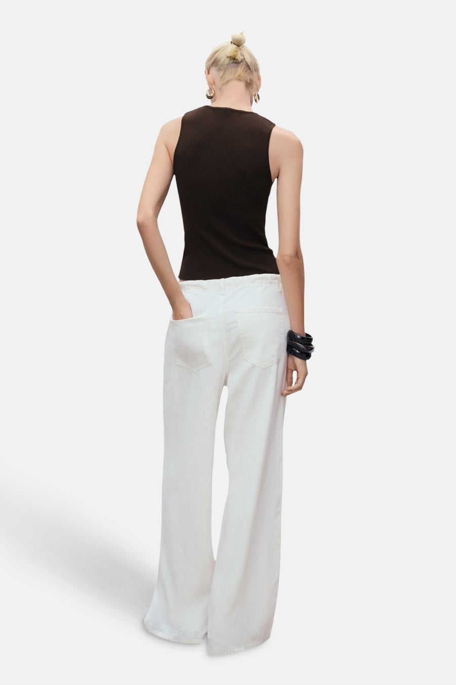 Top sans manches brun de MANGO, porté avec un pantalon blanc large et un bracelet noir.
