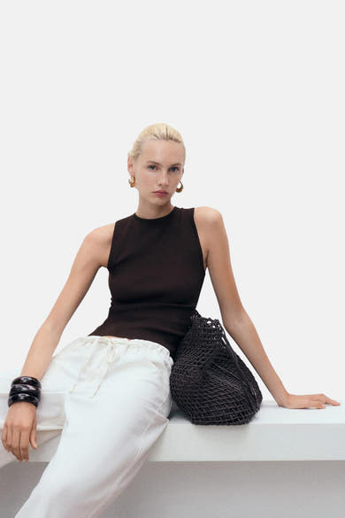 Top sans manches brun de MANGO, porté avec un pantalon blanc et des bijoux noirs.