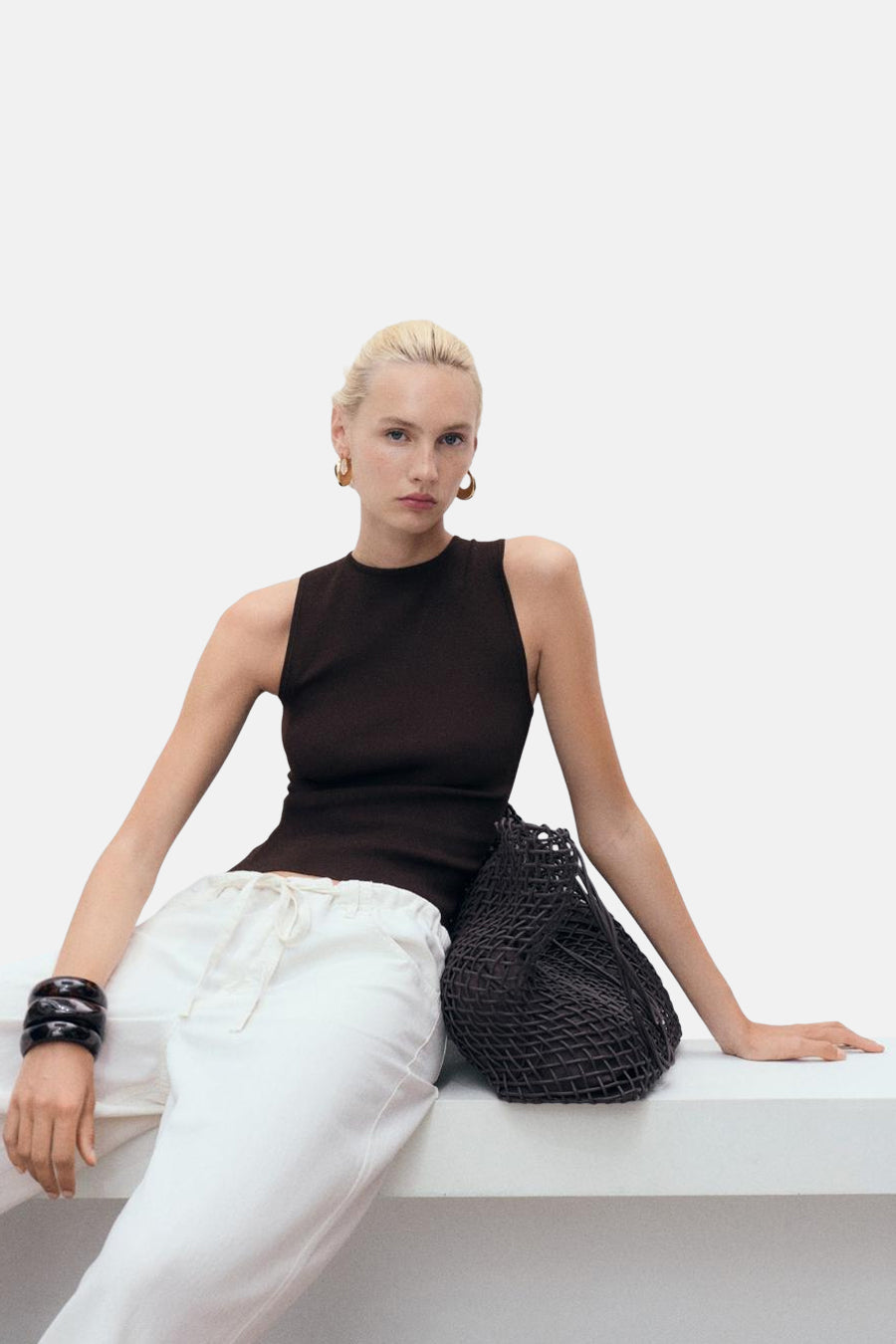 Top sans manches brun de MANGO, porté avec un pantalon blanc et des bijoux noirs.