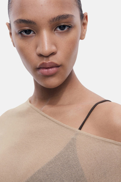 Pull à col rond beige de MANGO, avec une bretelle de soutien-gorge marron visible.