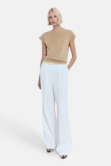 Beige mouwloze top van MANGO, gedragen met een gouden riem en een witte broek met wijde pijpen.