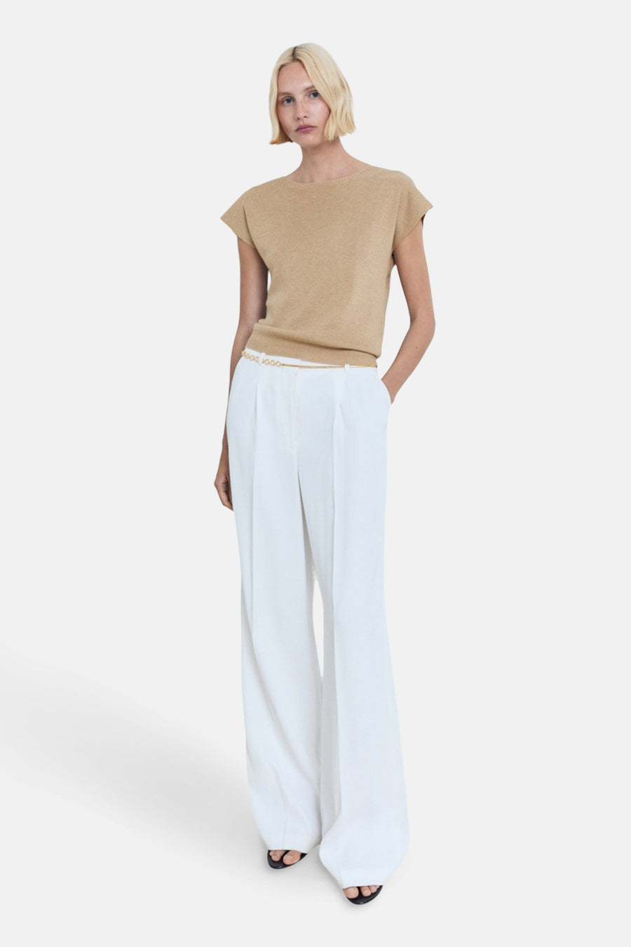 Beige mouwloze top van MANGO, gedragen met een gouden riem en een witte broek met wijde pijpen.