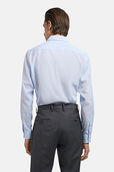 Blauwe blouse met lange mouwen van MANGO, van achteren gezien, gedragen met een grijze pantalon.