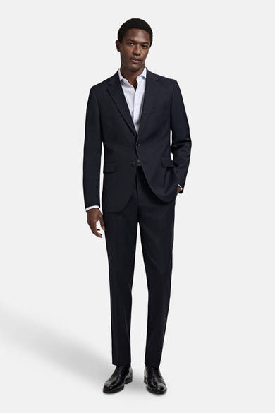 Blauwe blazer van MANGO, slim fit, twee knopen, ingesneden revers en klepzakken. Gedragen met een bijpassende broek, wit overhemd en zwarte schoenen.