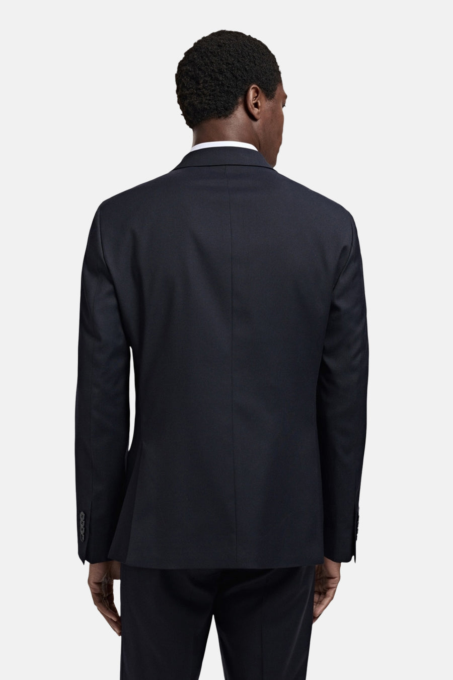 Marineblauwe blazer van MANGO, van achteren gezien op een man, met witte kraag, 4 knopen op de manchetten en donkere broek.