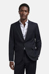 Blauwe blazer van MANGO gedragen door een man met een gestreept, open overhemd en de hand in zijn zak.