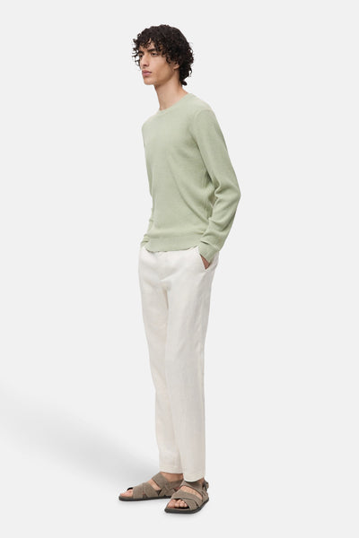 Pull à col rond vert de MANGO, en maille côtelée, porté avec un pantalon en lin écru et des sandales.