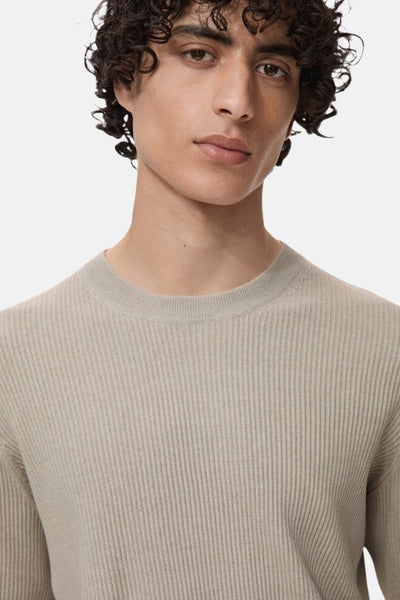 Beige ronde hals trui van MANGO in ribgebreide stof, gedragen door een man met krullend haar.