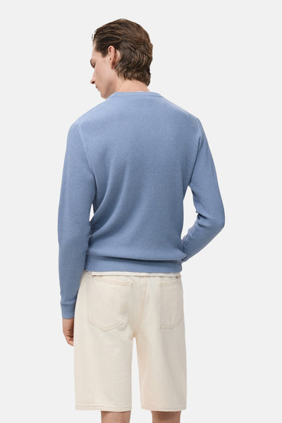 Pull à col rond bleu en maille côtelée de MANGO, porté avec un short en jean clair, vue de dos.
