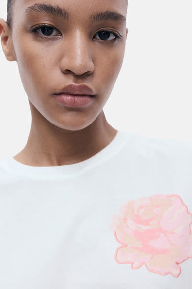 Wit T-shirt met korte mouwen van MANGO, versierd met een roze geborduurde bloem op de voorkant.