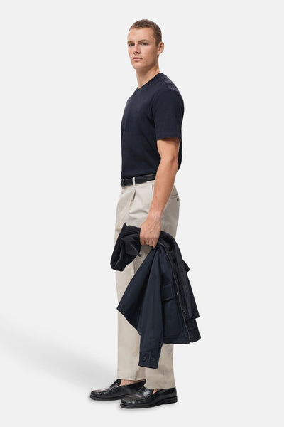Blauwe T-shirt met korte mouwen van MANGO, gedragen met een beige broek en zwarte loafers, met een jas in de hand.