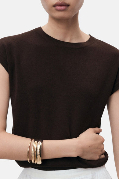 Bruin mouwloos topje van MANGO, gedragen met gouden armbanden en een witte rok.