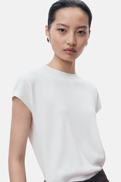 Top blanc en tricot de MANGO, porté avec des boucles d'oreilles rondes contrastées.