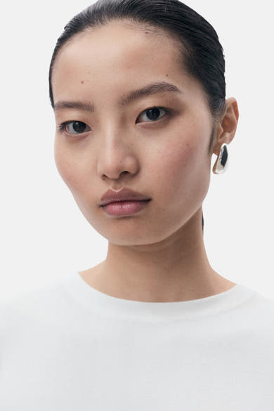 Top blanc de MANGO, porté avec des boucles d'oreilles argentées.