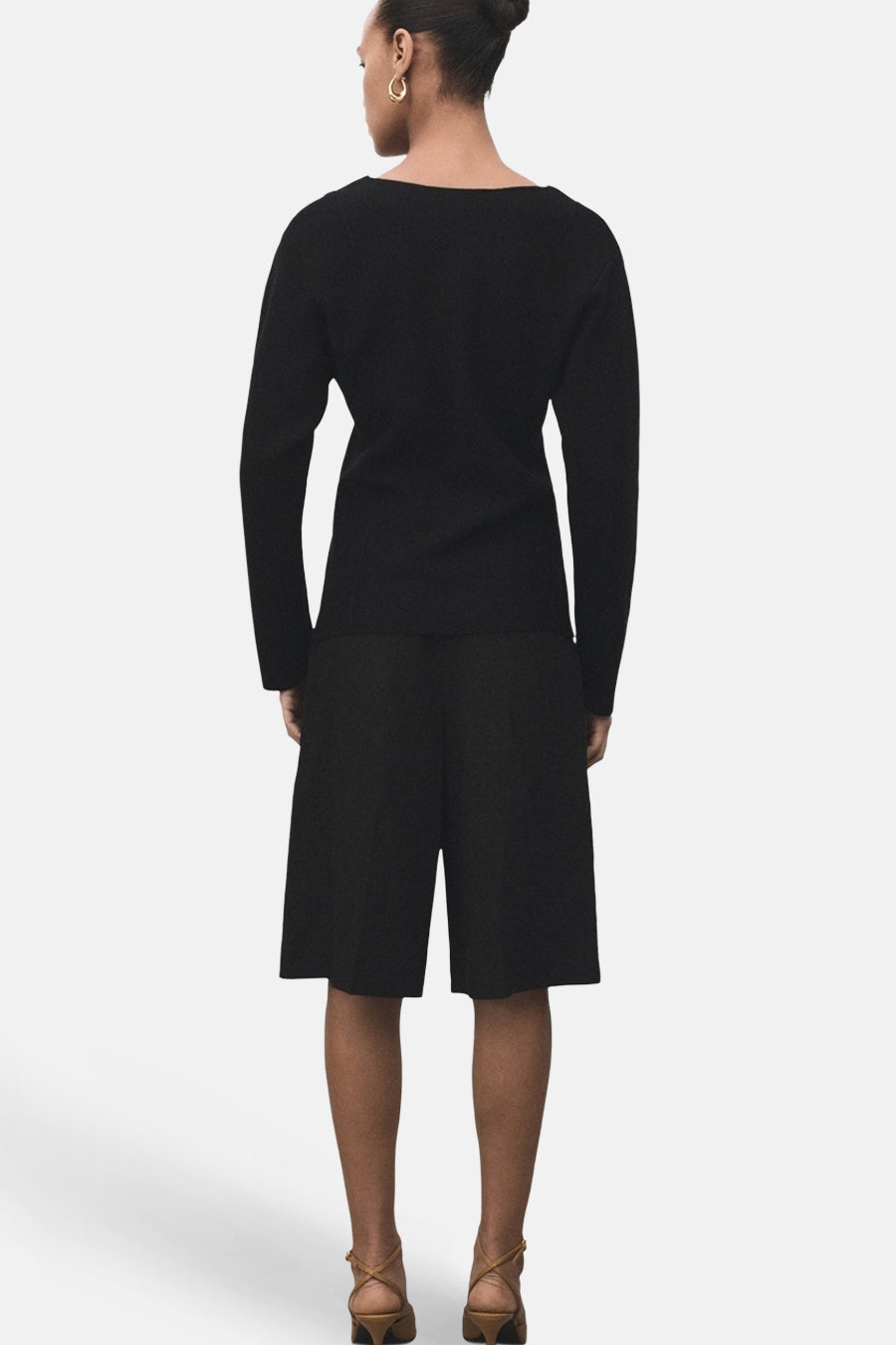 Cardigan noir de MANGO, porté avec un short noir et des chaussures à talons marron, vue de dos.
