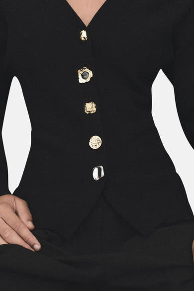 Cardigan noir par MANGO, avec une rangée de boutons décoratifs dorés et argentés.

