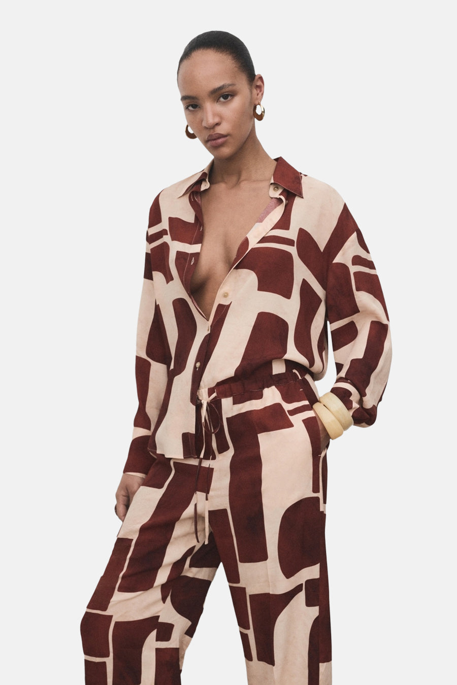 Multikleurige broek van MANGO, met een geometrische bruin-beige print, gedragen met een bijpassend open overhemd.