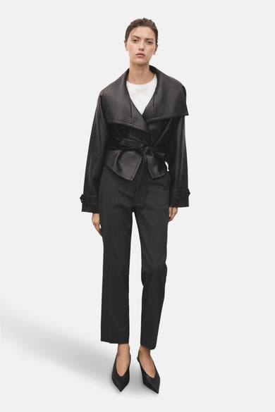 Pantalon gris à rayures de MANGO, porté avec un haut blanc et une veste noire nouée.
