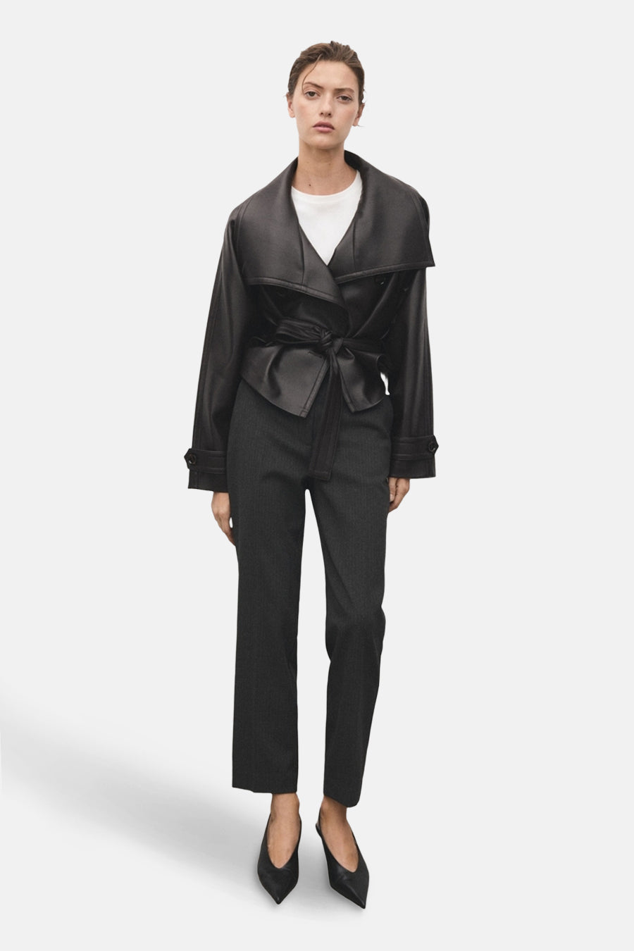 Pantalon gris à rayures de MANGO, porté avec un haut blanc et une veste noire nouée.
