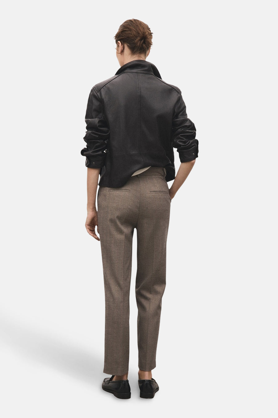 Pantalon brun de MANGO, avec une texture subtile et une coupe ajustée, porté avec une veste en cuir noire.