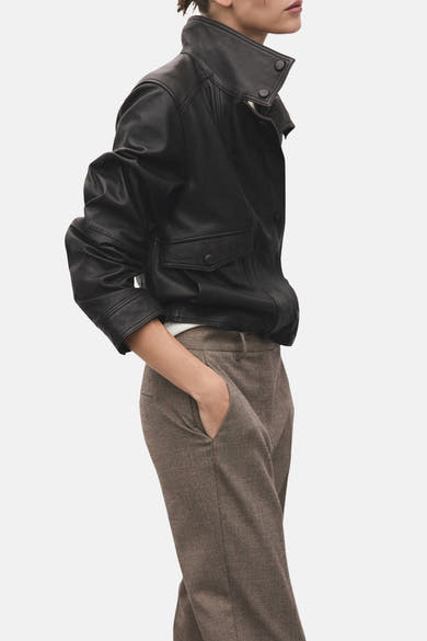 Pantalon brun de MANGO, porté avec une veste en cuir noire et les mains dans les poches.