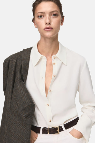 Ecru blouse met lange mouwen van MANGO, gedragen met een geruite jas en een bruine leren riem.