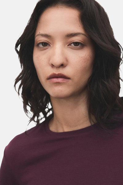 T-shirt bordeaux à manches longues de MANGO, porté par une femme avec des cheveux ondulés foncés.