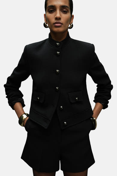 Blazer noir de MANGO avec fermeture boutonnée, poches à rabat et bijoux dorés.