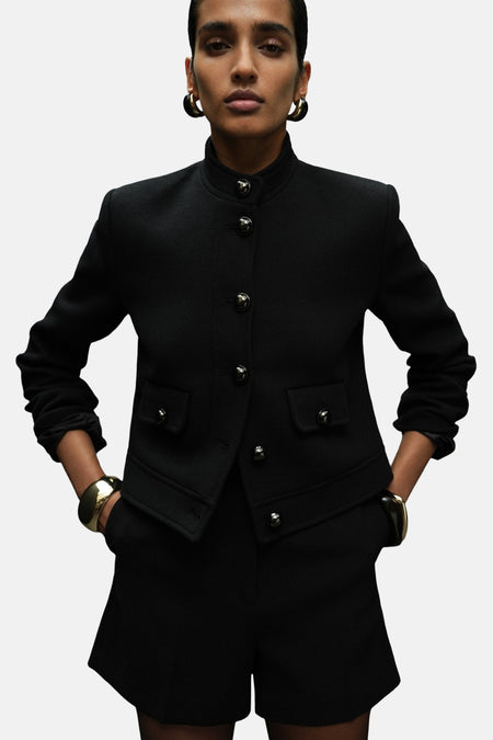 Zwarte blazer van MANGO met knoopsluiting, klepzakken en gouden sieraden.