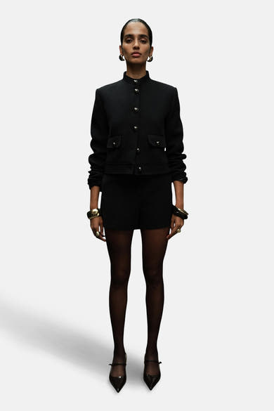 Blazer noir de MANGO avec boutons dorés et porté avec des shorts et des bijoux dorés.