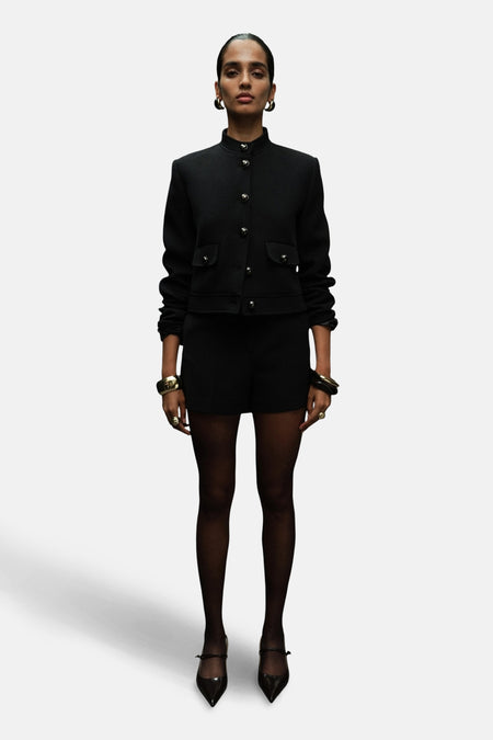 Zwarte blazer van MANGO met gouden knopen, gedragen met een korte broek en gouden sieraden.
