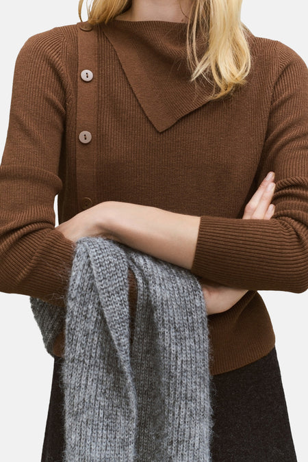 Pull à col rond brun de MANGO avec boutonnage asymétrique, porté avec une écharpe grise.
