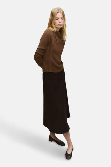 Pull à col rond brun de MANGO, porté avec une jupe longue foncée et des chaussures plates.