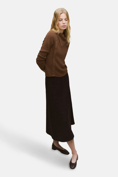Pull à col rond brun de MANGO, porté avec une jupe longue foncée et des chaussures plates.