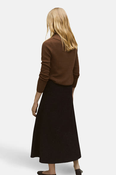 Pull à col rond marron de MANGO, porté avec une jupe noire évasée et des chaussures plates, vue de dos.