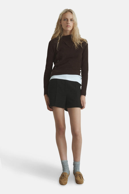 Pull à col rond brun de MANGO, porté avec un short noir et des chaussures bateau marron.
